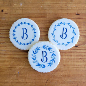 Custom cookies with blue floral designs and the letter B on a wooden surface.