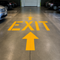 Yellow 'EXIT' sign with an arrow on a concrete floor in a parking garage.