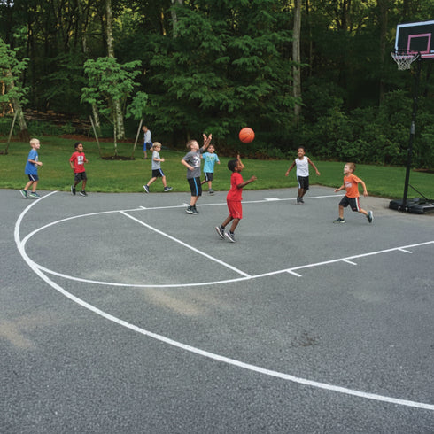 Children playing basketball on an outdoor court with trees in the background