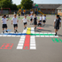 Children playing hopscotch on a playground with colorful grid markings.