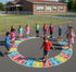 Children playing on a colorful alphabet-themed playground surface in front of a school building.