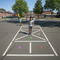 Children playing hopscotch on a school playground with colorful markings.