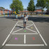 Children playing hopscotch on a school playground with colorful markings.