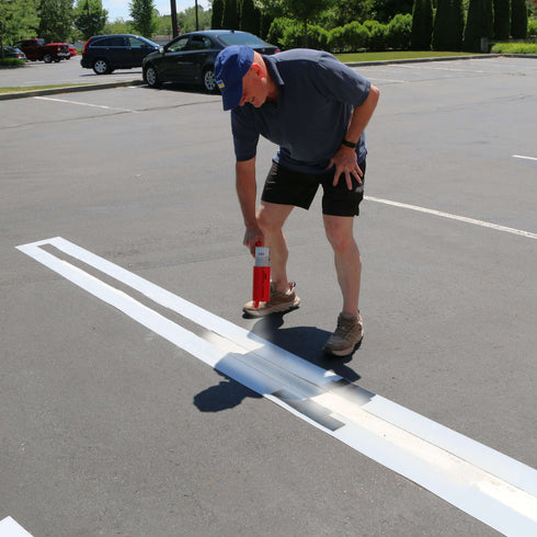 A man using line stencils to paint parking lot lines, demonstrating easy application for precise markings.