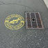 Circular logo with a fish illustration and 'No Dumping Drains to River' text applied in yellow onto pavement.