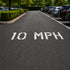 10 MPH speed limit sign on a road with parked cars in the background