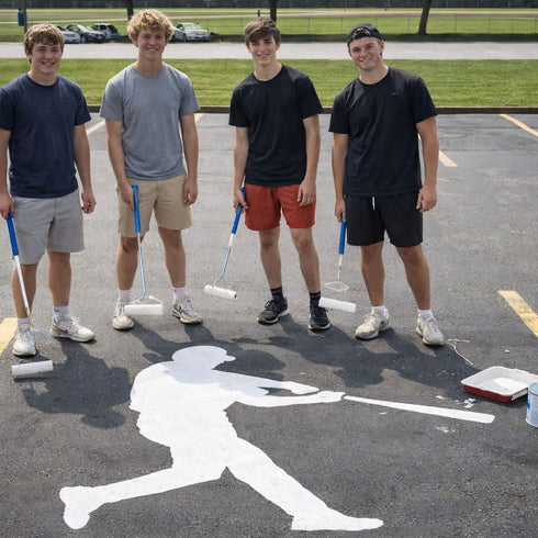 Four young men standing on a parking lot with brooms, next to a white silhouette of a baseball player.
