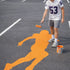 Person painting an orange outline of a person on a gray surface