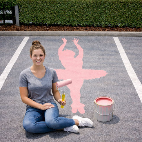 High School senior sitting on a parking lot with a pink ballerina painted onto it.