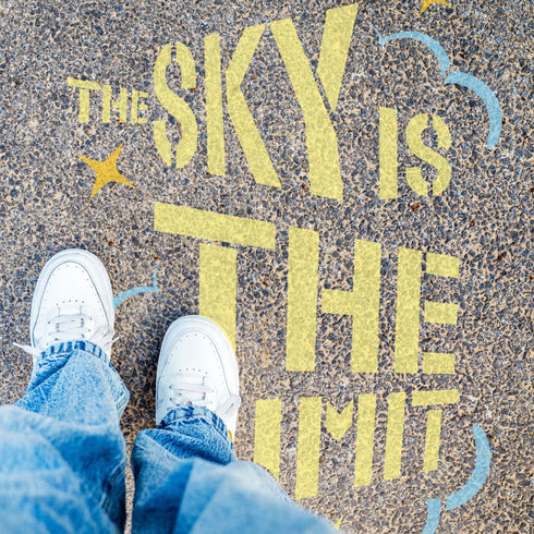 Person standing on pavement that has been stenciled with 'The Sky is the Limit' text.