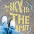 Person standing on pavement that has been stenciled with 'The Sky is the Limit' text.
