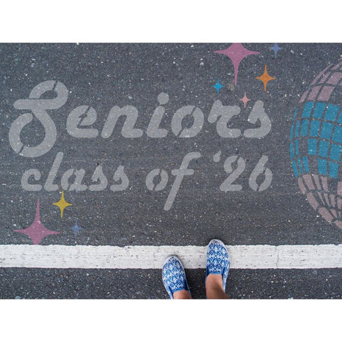 Person standing on pavement that has been stenciled with 'Seniors Class of '26' text.