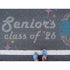 Person standing on pavement that has been stenciled with 'Seniors Class of '26' text.