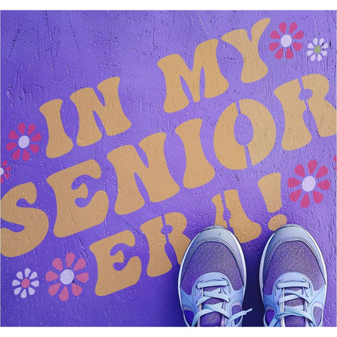 Person standing on pavement that has been stenciled with 'In My Senior Era!' text.