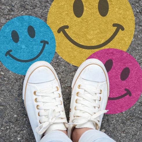 Person standing on pavement that has been stenciled with 2 smiley faces.