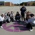 Group of people posing around a large purple peace symbol on the ground in a parking lot.