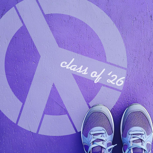 Person standing on pavement that has been stenciled with a peace sign and Class of '26.