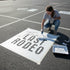 Person painting 'The Last Rodeo' on a large sheet of paper outdoors.
