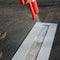 Spraying parking lot line stencil with red spray can for clear markings on asphalt surface.