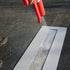 Spraying parking lot line stencil with red spray can for clear markings on asphalt surface.